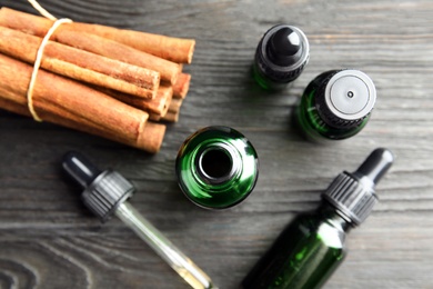 Photo of Bottles with essential oil and cinnamon sticks on black wooden table, flat lay