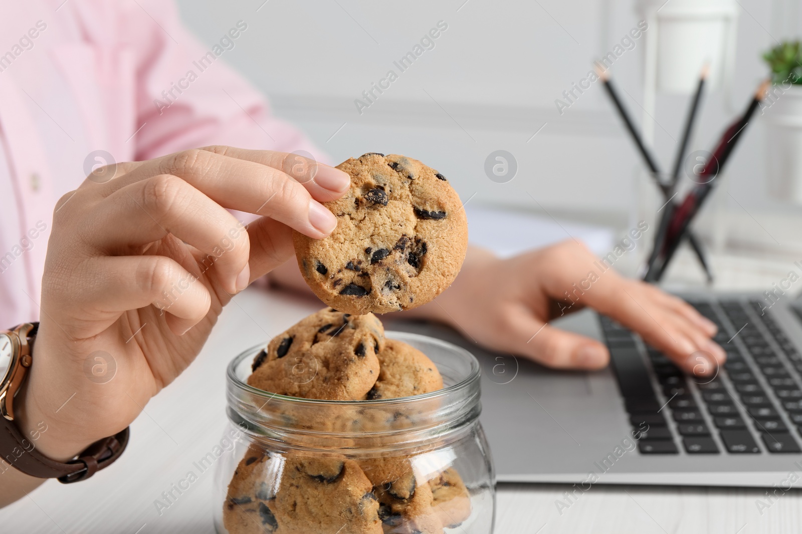 Photo of Office worker taking chocolate chip cookie from jar at workplace, closeup