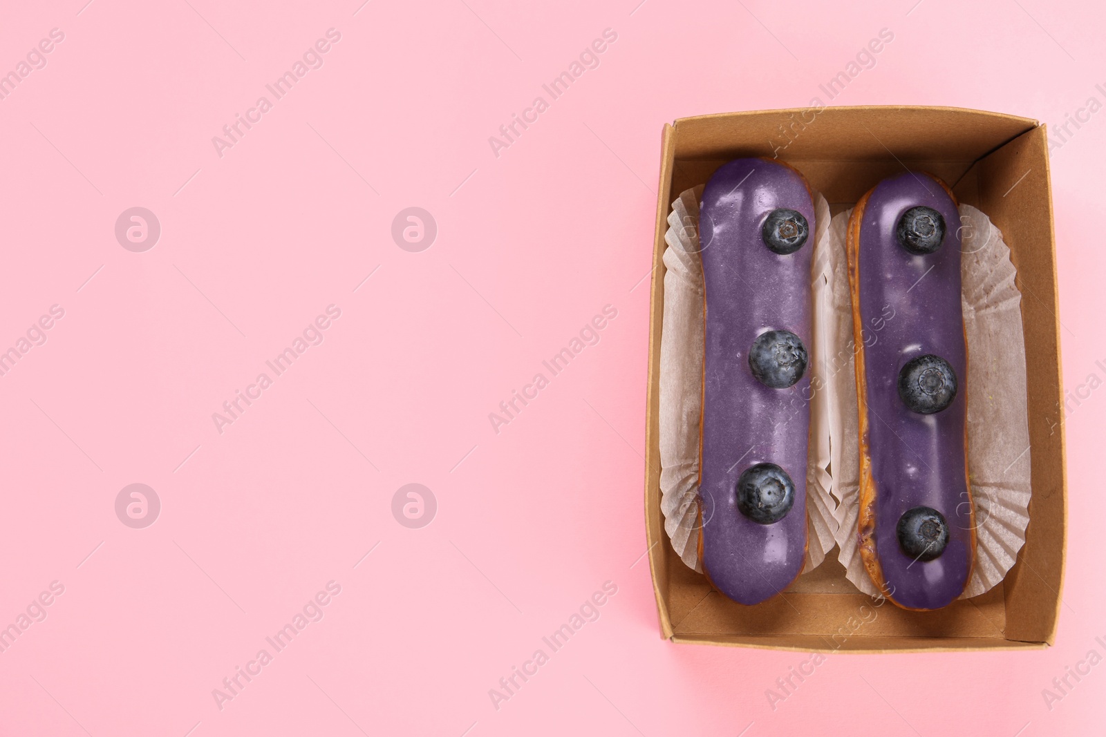 Photo of Delicious purple eclairs decorated with blueberries on pink background, top view. Space for text