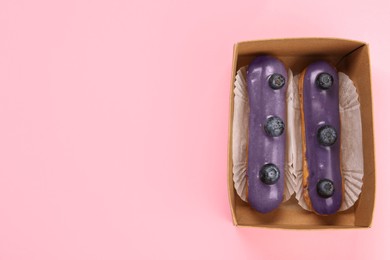 Delicious purple eclairs decorated with blueberries on pink background, top view. Space for text