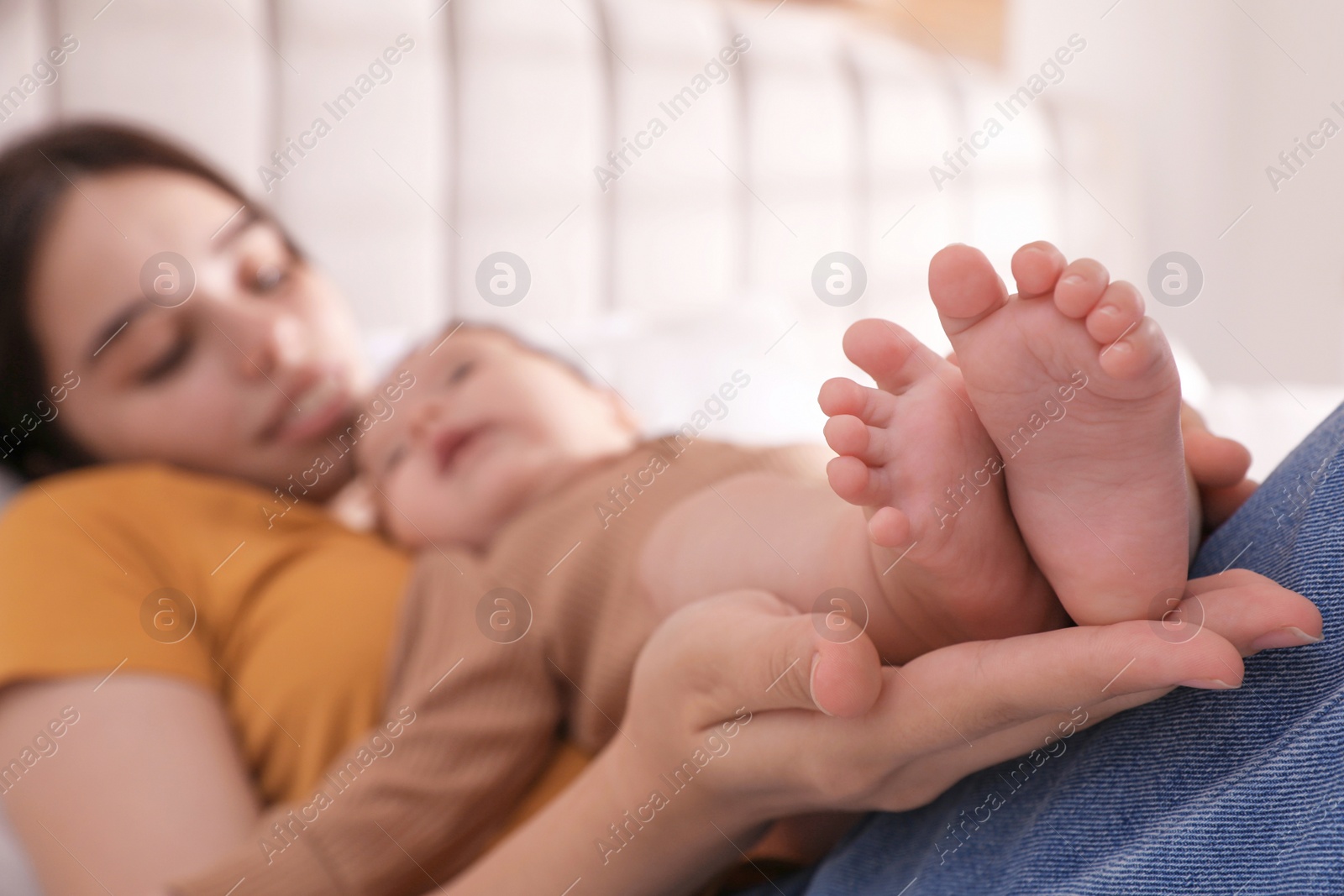 Photo of Happy young mother with her cute baby at home, focus on feet