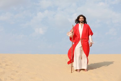 Jesus Christ walking with stick in desert. Space for text