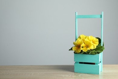 Photo of Beautiful yellow primula (primrose) flower in wooden crate on table, space for text. Spring blossom