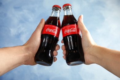 Photo of MYKOLAIV, UKRAINE - NOVEMBER 15, 2018: People with bottles of Coca Cola on color background, closeup