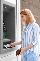 Photo of Beautiful woman taking money from cash machine outdoors
