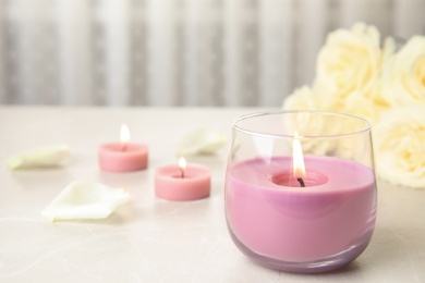Photo of Burning candle in glass holder and roses on light table, space for text