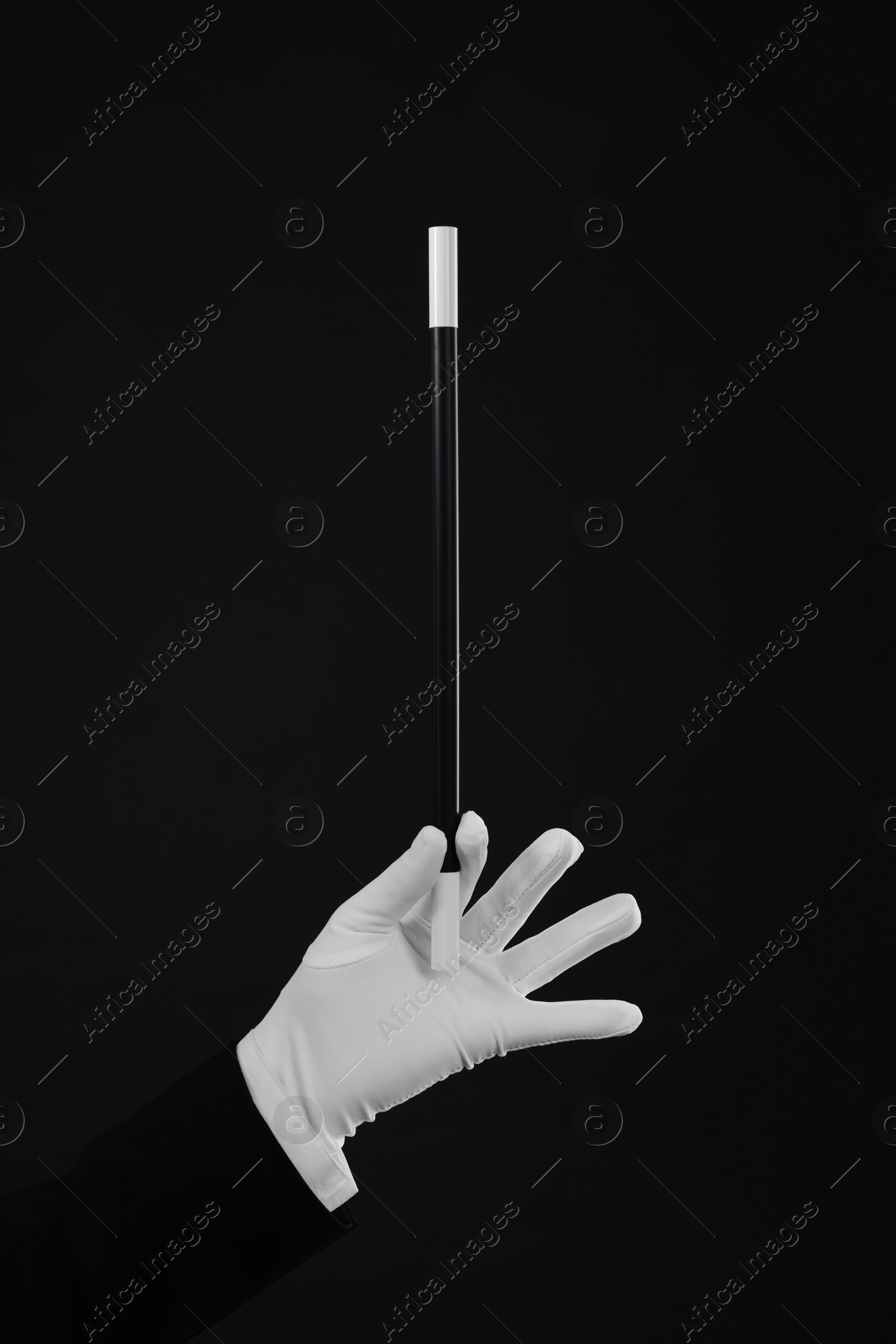 Photo of Magician holding wand on black background, closeup