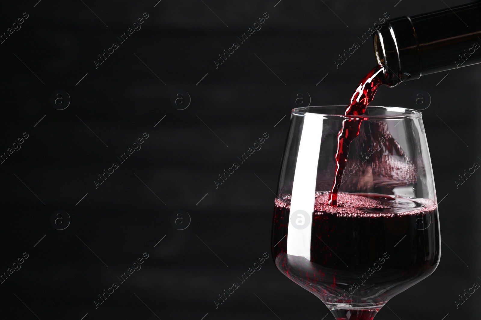 Photo of Pouring red wine into glass against dark background, closeup. Space for text