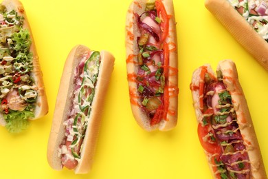 Photo of Delicious hot dogs with different toppings on yellow background, flat lay