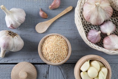 Photo of Dehydrated garlic granules and fresh bulbs on grey wooden table, flat lay