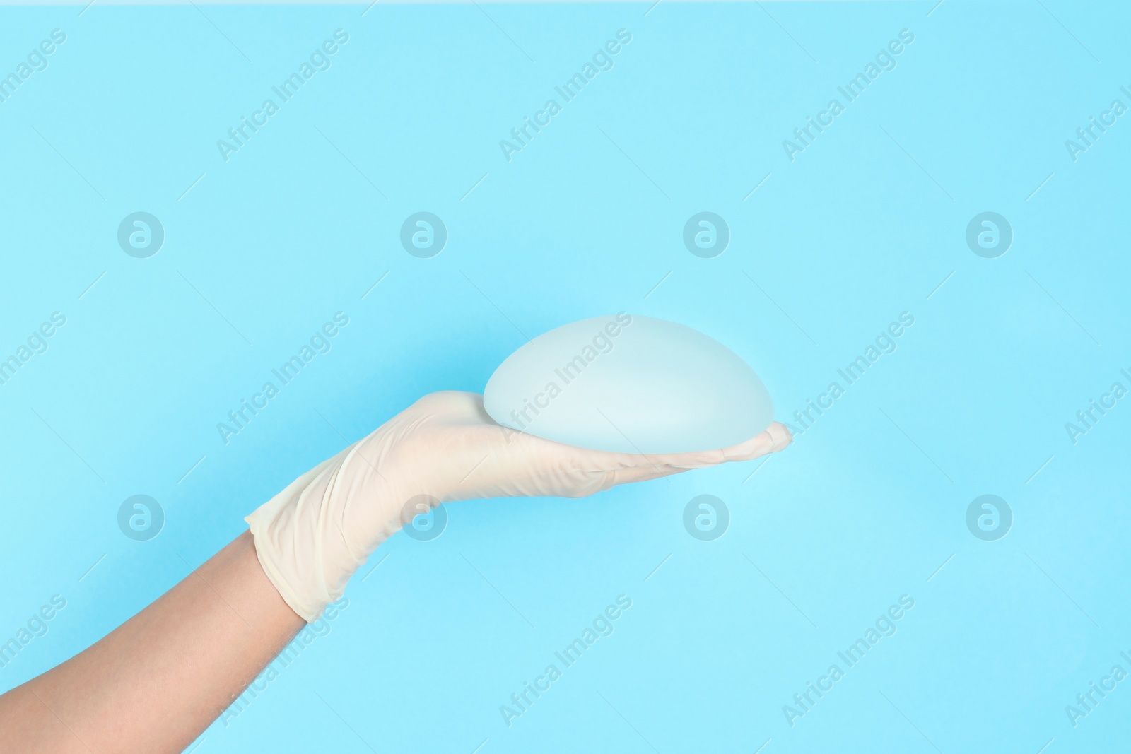 Photo of Doctor holding silicone implant for breast augmentation on color background, space for text. Cosmetic surgery