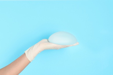 Photo of Doctor holding silicone implant for breast augmentation on color background, space for text. Cosmetic surgery