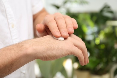 Photo of Man applying moisturizing cream onto hand on blurred background, closeup