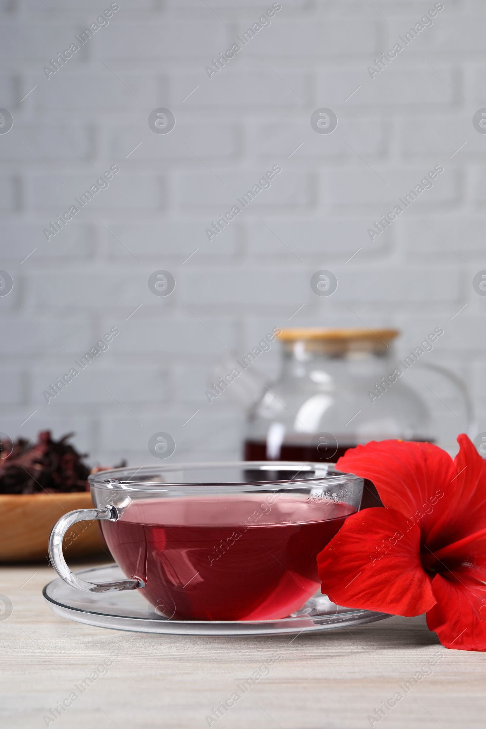 Photo of Delicious hibiscus tea and beautiful flower on light wooden table, space for text