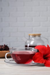 Delicious hibiscus tea and beautiful flower on light wooden table, space for text