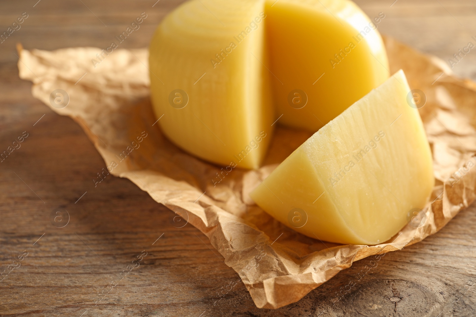 Photo of Parchment paper with cut wheel of delicious cheese on wooden table, closeup