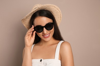 Photo of Beautiful young woman with straw hat and sunglasses on beige background. Stylish headdress