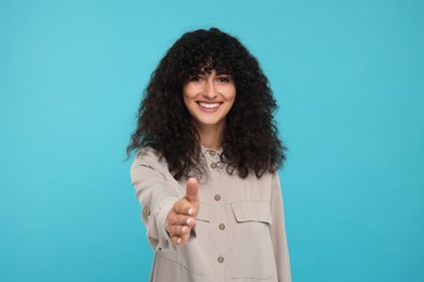Photo of Happy young woman welcoming and offering handshake on light blue background