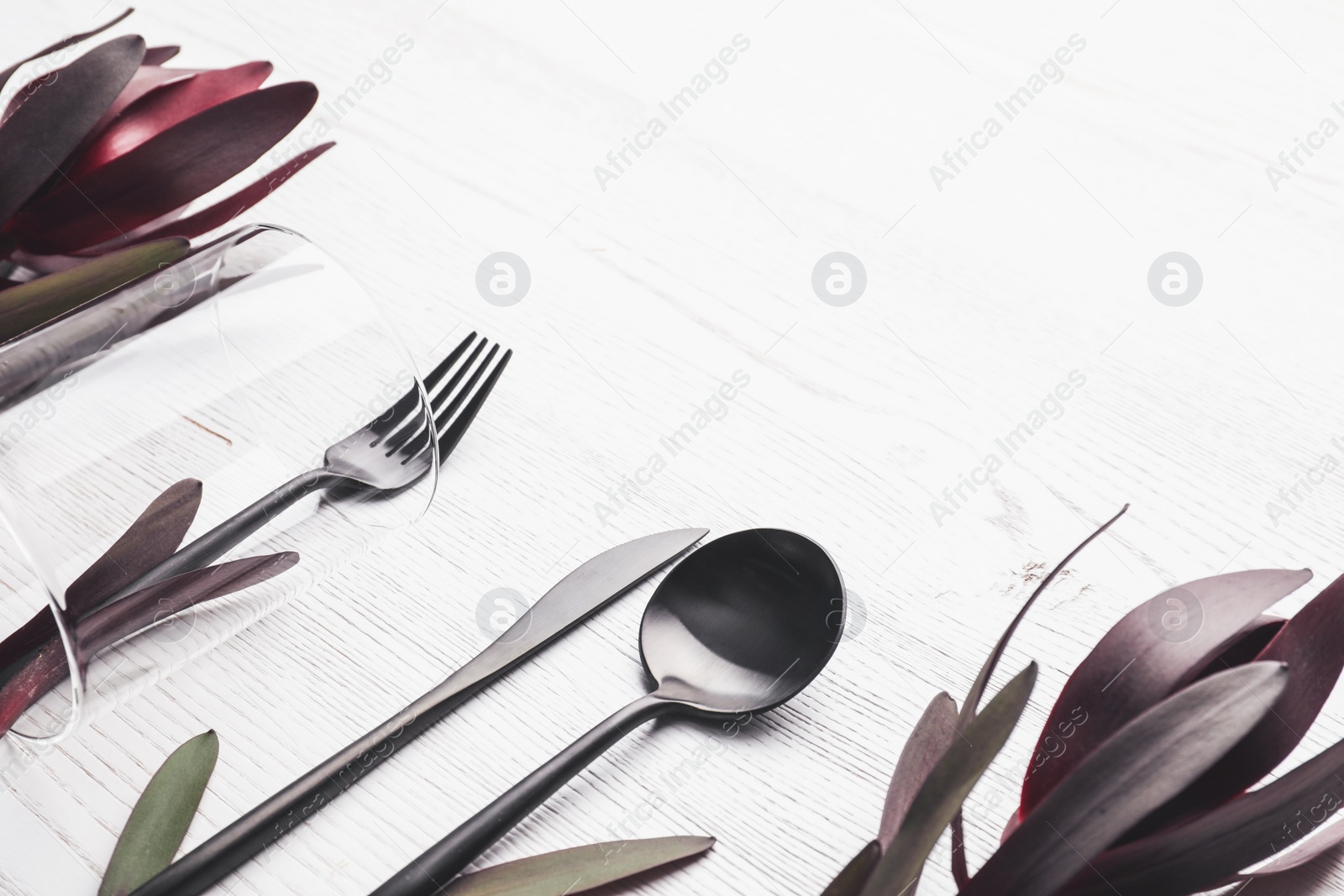 Photo of Cutlery and floral decor on white wooden background, space for text. Table setting elements