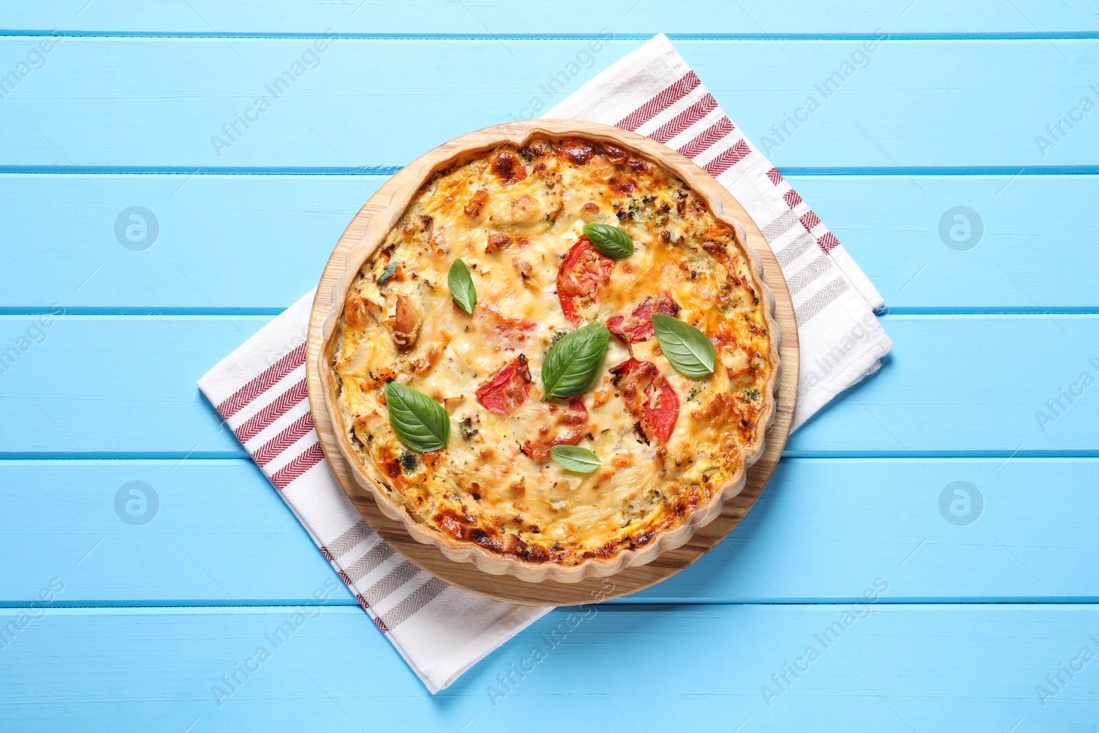 Photo of Tasty quiche with tomatoes, basil and cheese served on light blue wooden table, top view