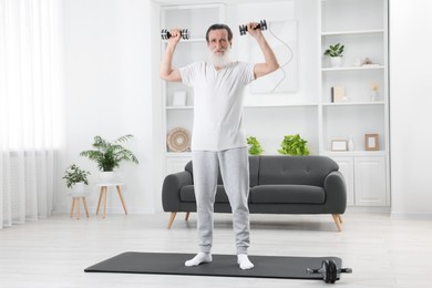 Photo of Senior man exercising with dumbbells on mat at home. Sports equipment