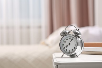 Photo of Silver alarm clock on white nightstand indoors. Space for text