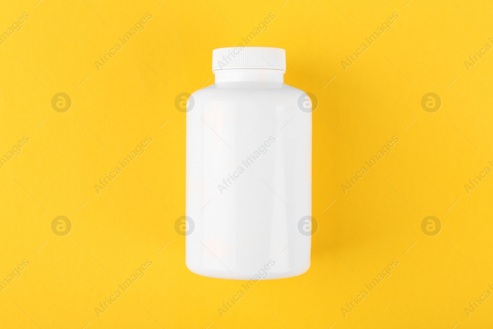 Photo of One white medical bottle on yellow background, top view