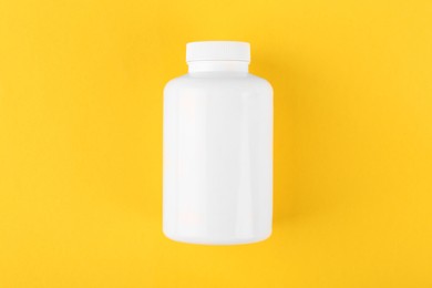 Photo of One white medical bottle on yellow background, top view