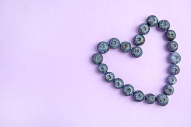 Photo of Heart of fresh ripe blueberries on lilac background, flat lay. Space for text