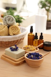 Photo of Soap bar, dry flowers, bottles of essential oils and towels on wooden table indoors. Spa time