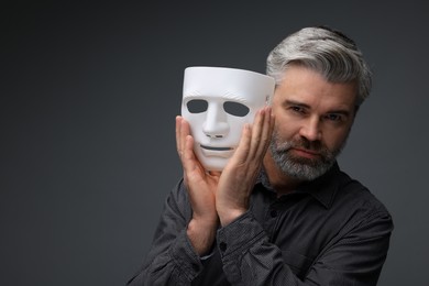 Photo of Multiple personality concept. Man with mask on dark grey background, space for text