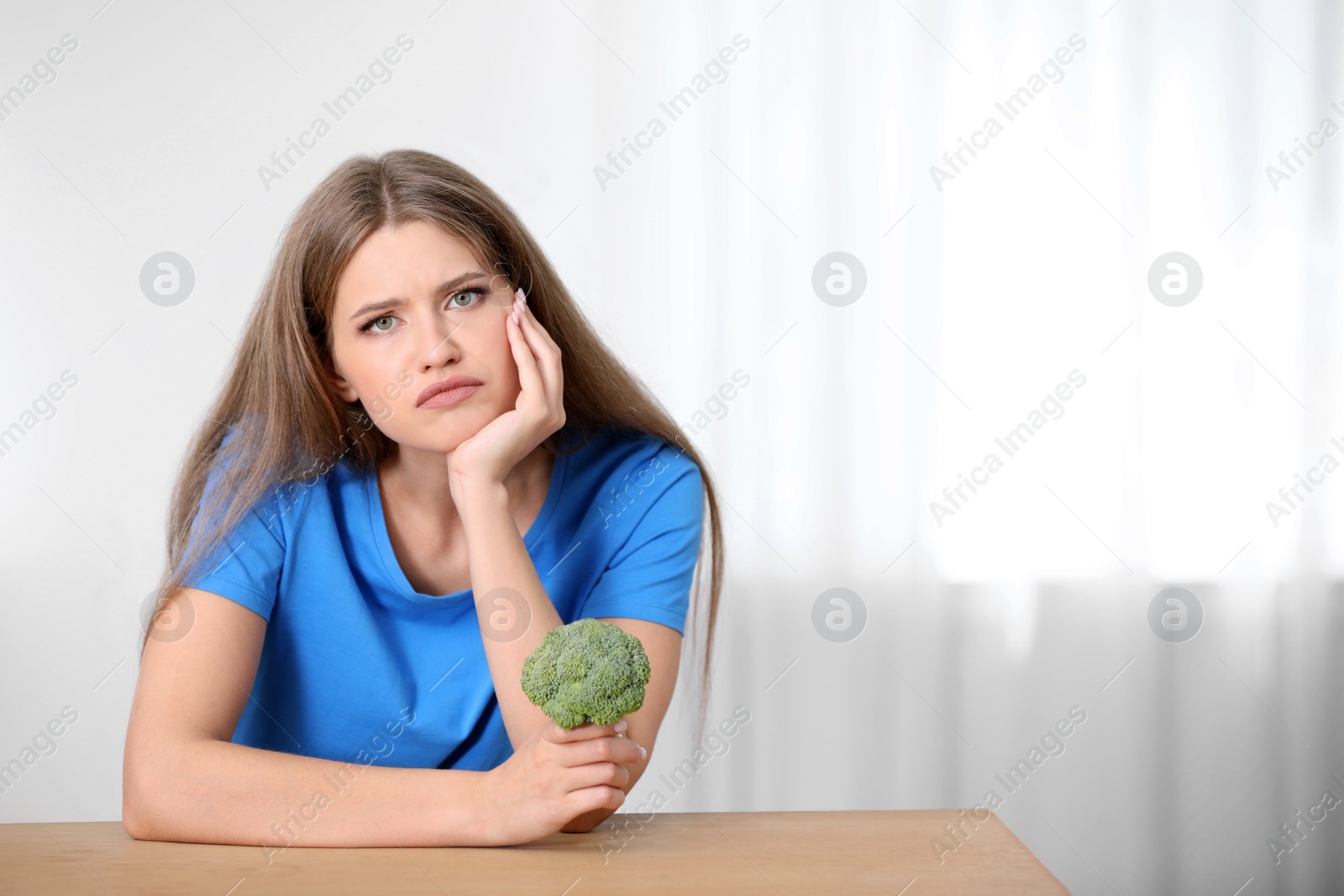 Photo of Portrait of unhappy woman with broccoli at table indoors