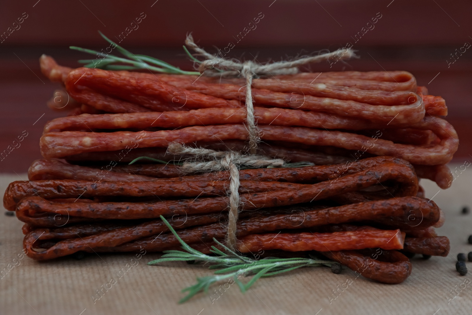 Photo of Tasty dry cured sausages (kabanosy) and spices on parchment paper, closeup