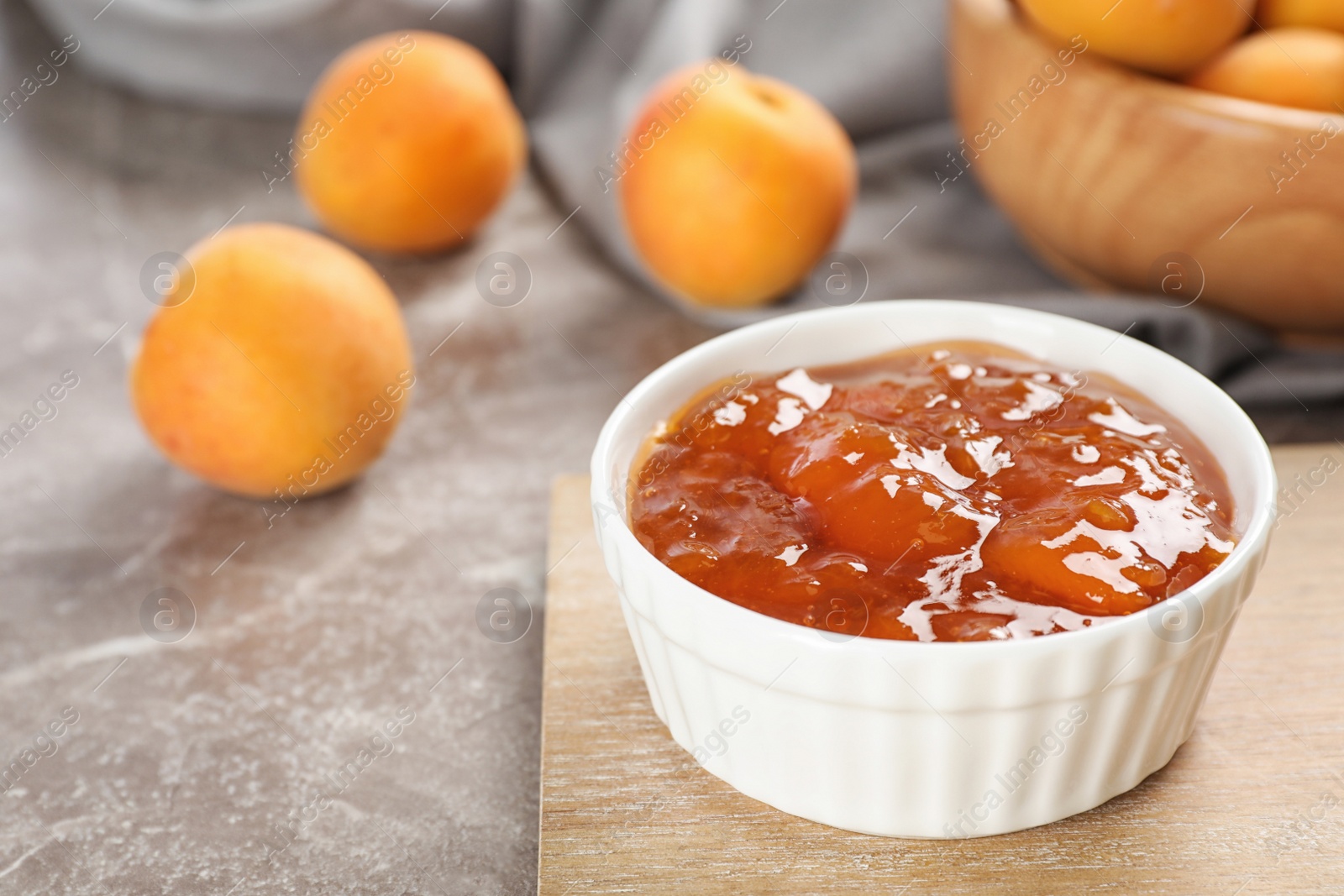 Photo of Bowl with tasty apricot jam on wooden board