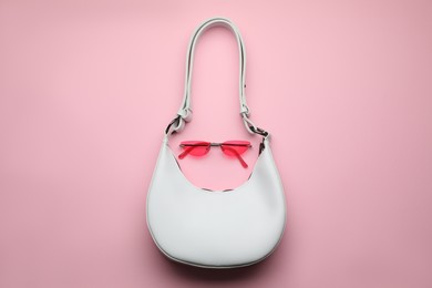 Stylish woman's bag and sunglasses on pink background, top view