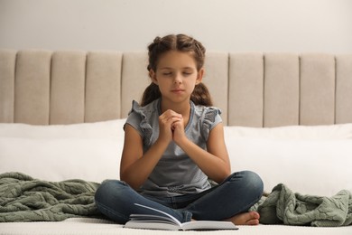 Photo of Cute little girl praying over Bible in bedroom