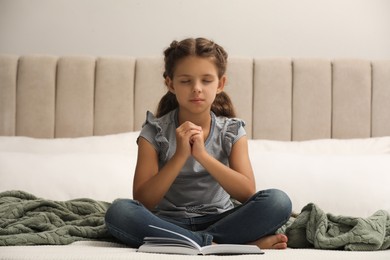 Cute little girl praying over Bible in bedroom