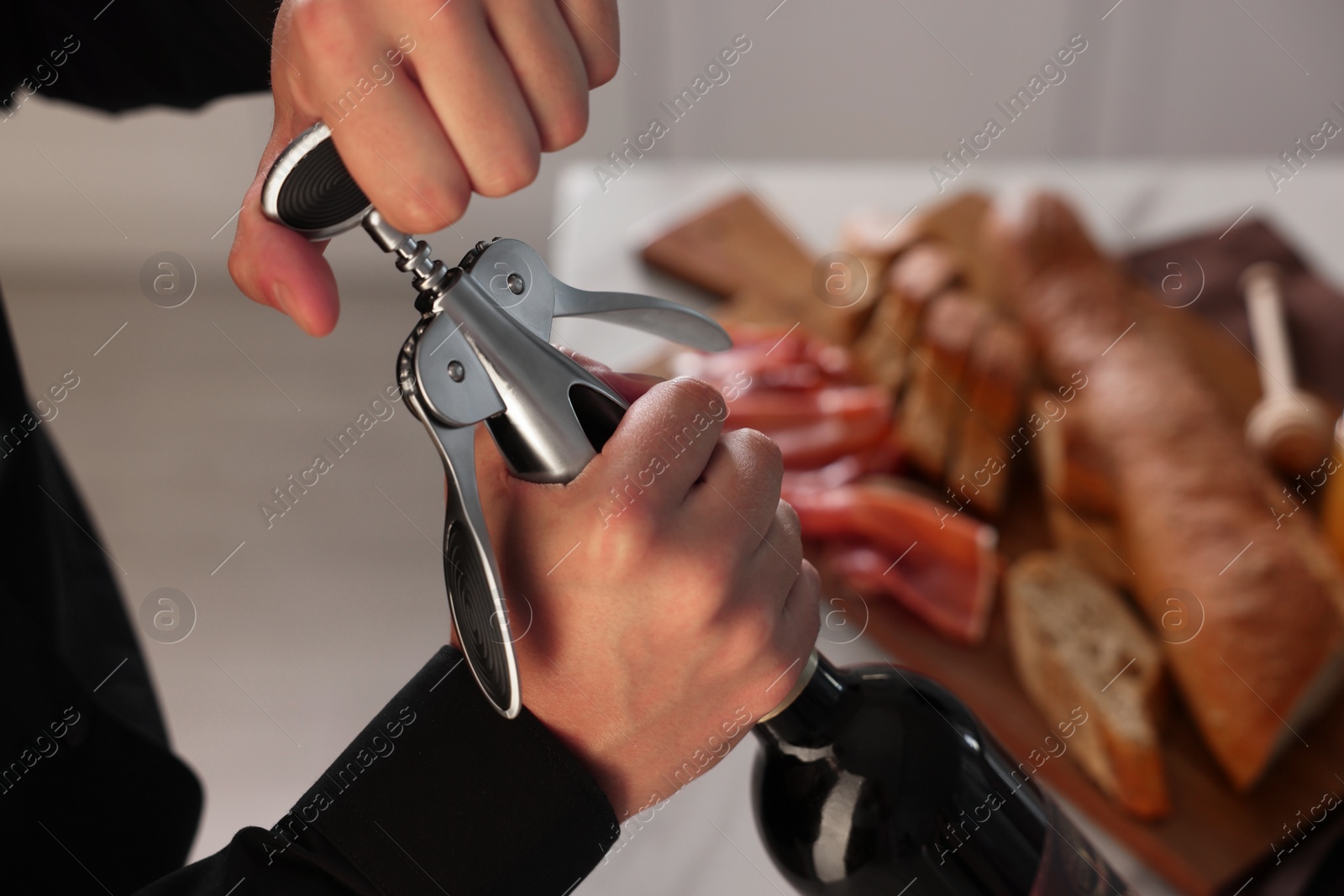 Photo of Romantic dinner. Man opening wine bottle with corkscrew indoors, closeup