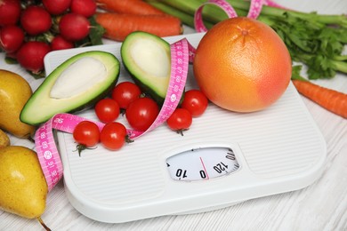 Photo of Scales, healthy food and measuring tape on white wooden table