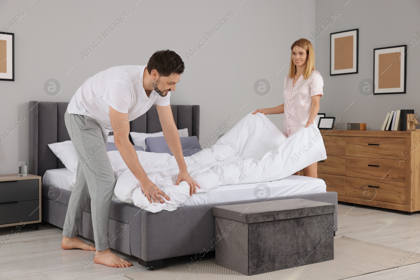 Photo of Couple changing bed linens in room. Domestic chores