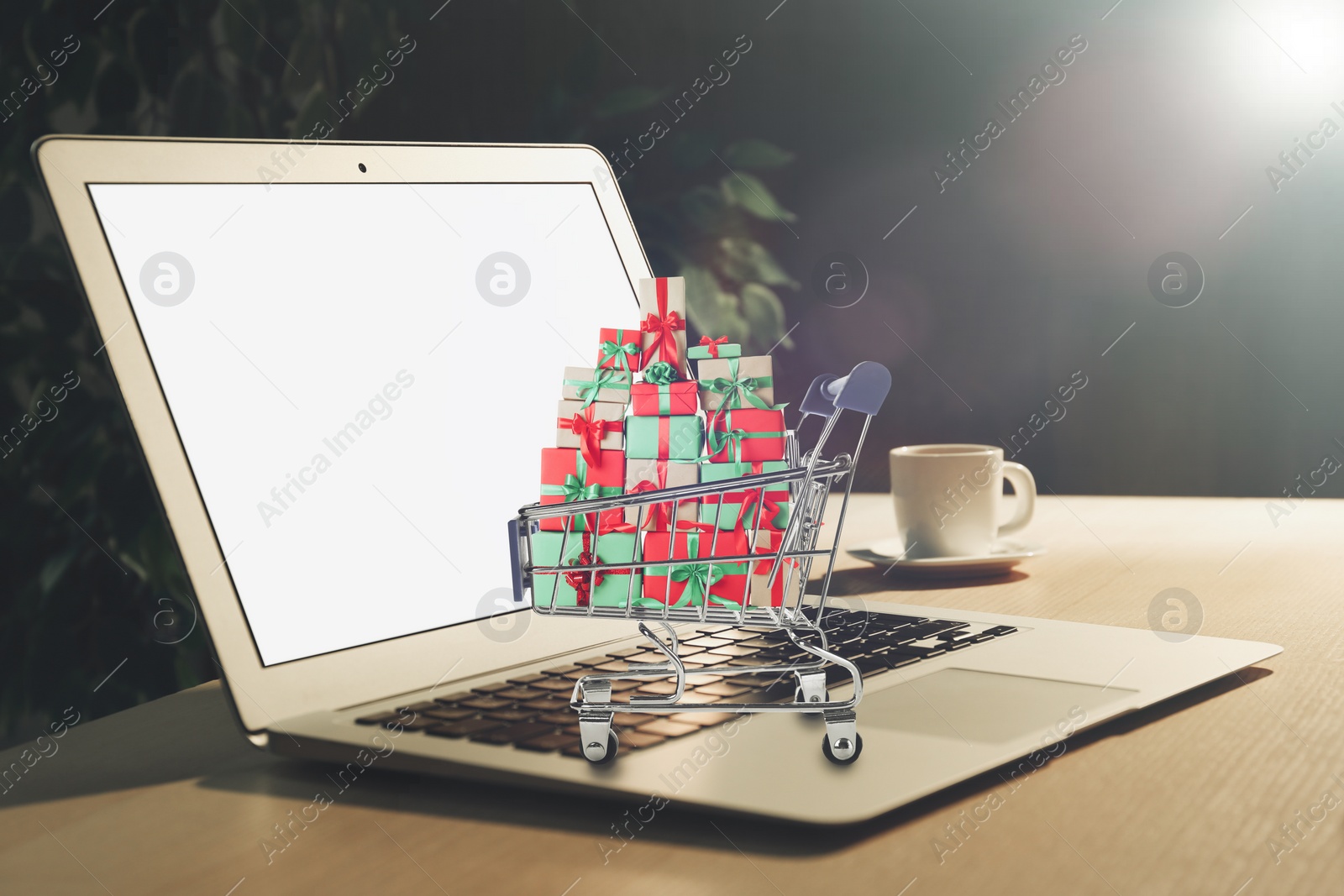 Image of Online shopping. Modern laptop and small cart with boxes on table