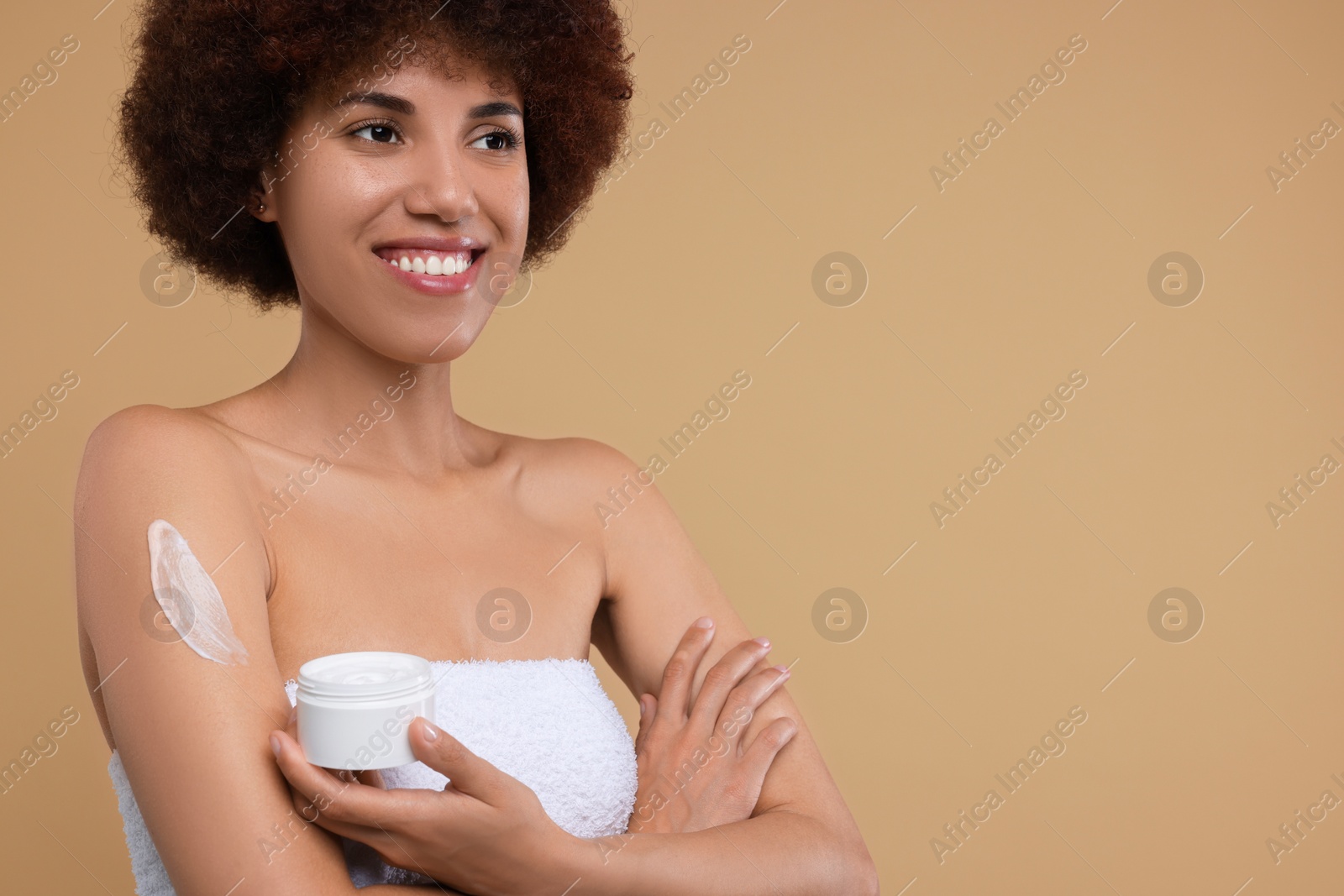 Photo of Beautiful young woman applying body cream onto arm on beige background, space for text