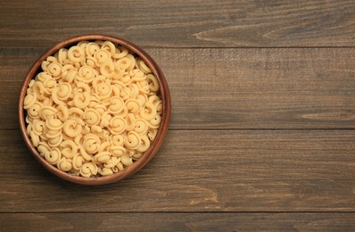 Photo of Raw dischi volanti pasta in bowl on wooden table, top view. Space for text