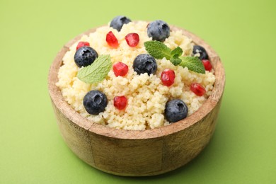 Photo of Bowl of tasty couscous with blueberries, pomegranate and mint on green background, closeup