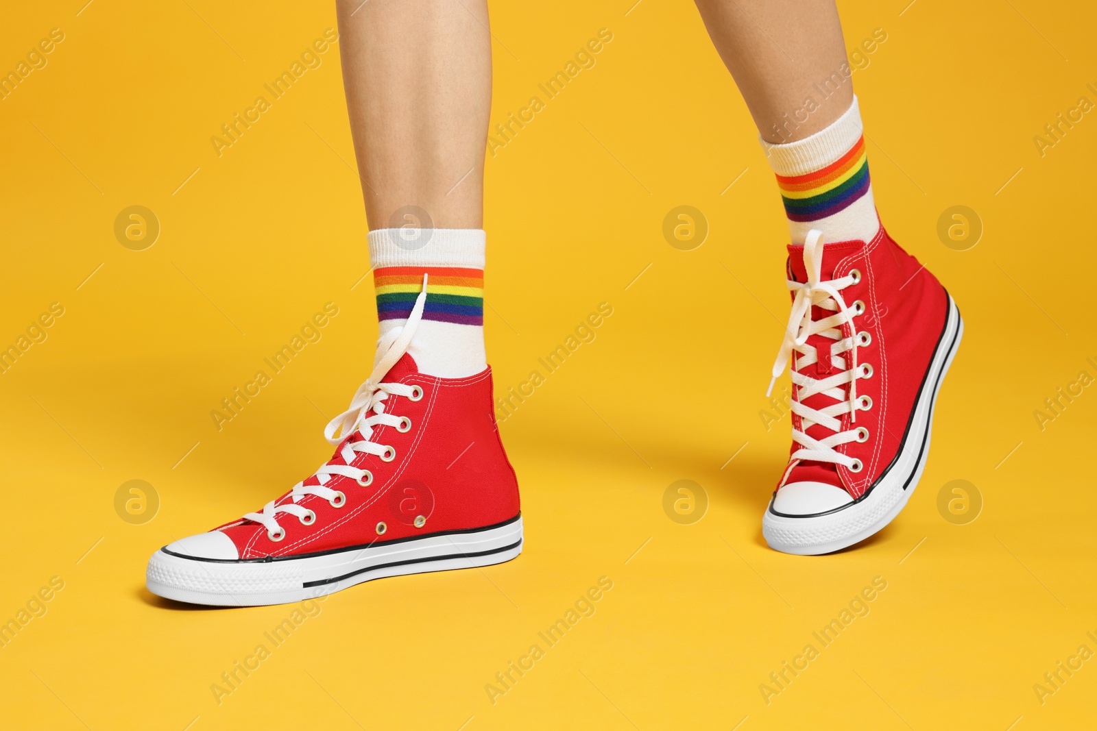 Photo of Woman in stylish gumshoes on yellow background, closeup