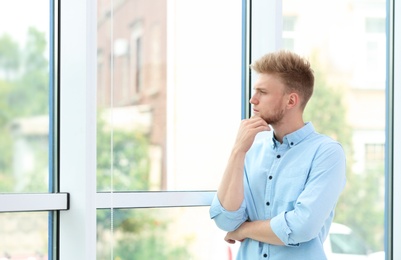 Portrait of handsome young man looking out window indoors