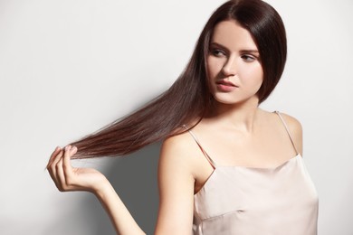 Portrait of beautiful young woman with healthy strong hair on light gray background