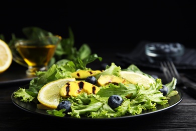 Photo of Delicious avocado salad with lemon and blueberries on black wooden table