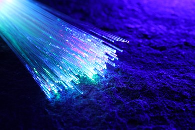 Optical fiber strands transmitting different color lights on textured background, closeup. Space for text