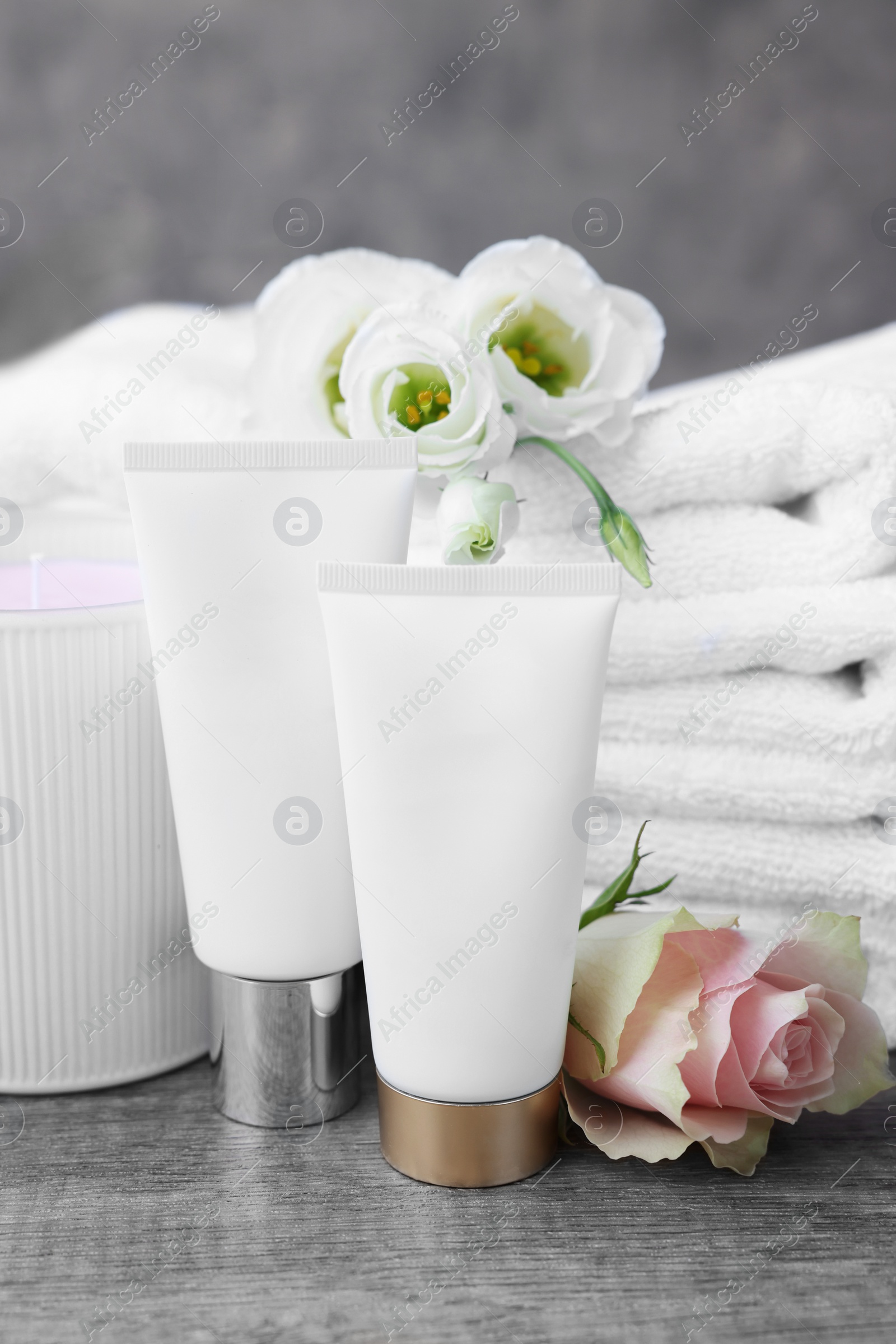 Photo of Cosmetic products, scented candle and folded towels with flowers on wooden table indoors